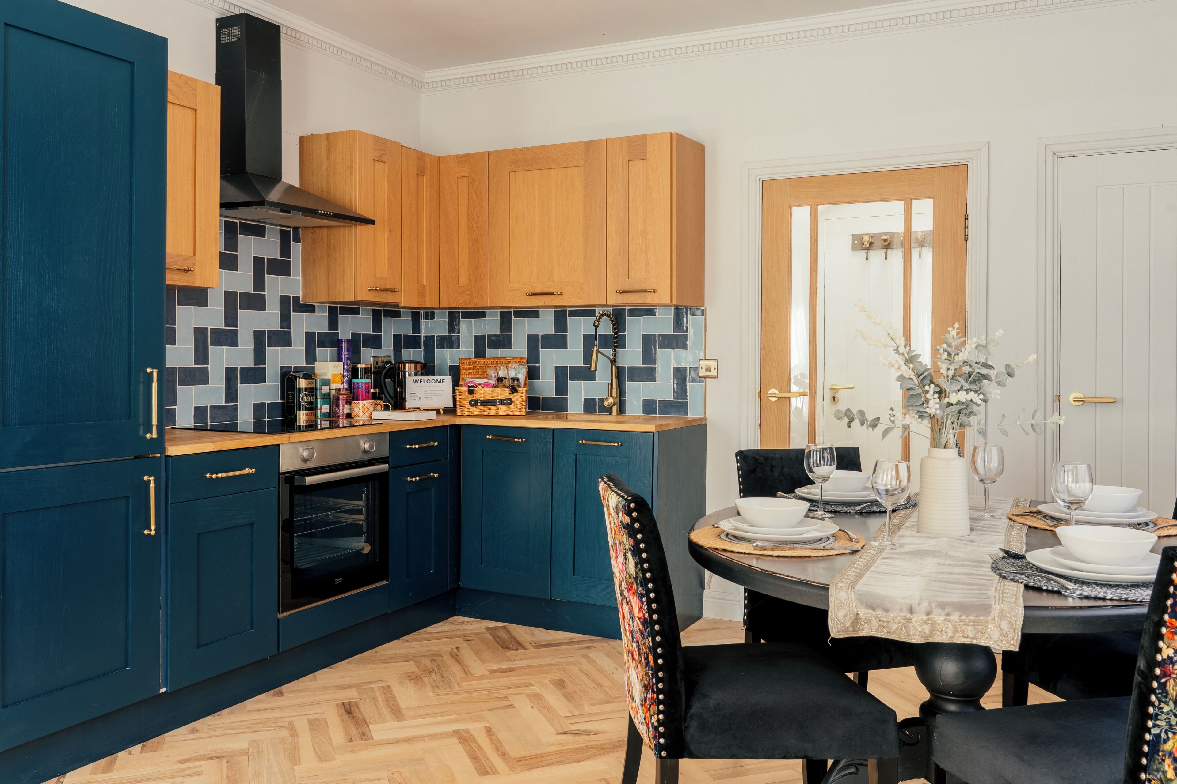 A modern kitchen with wooden cabinets, a herringbone floor, and a dining area with a table set for four.