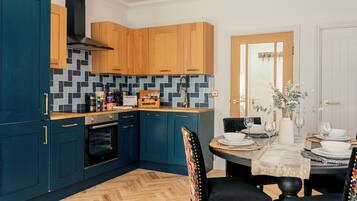A modern kitchen with wooden cabinets, a herringbone floor, and a dining area with a table set for four.