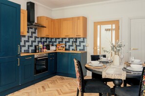 A modern kitchen with wooden cabinets, a herringbone floor, and a dining area with a table set for four. - Gorgeous Central 2BR Apt + Free Parking I Walk to town (Harrogate)