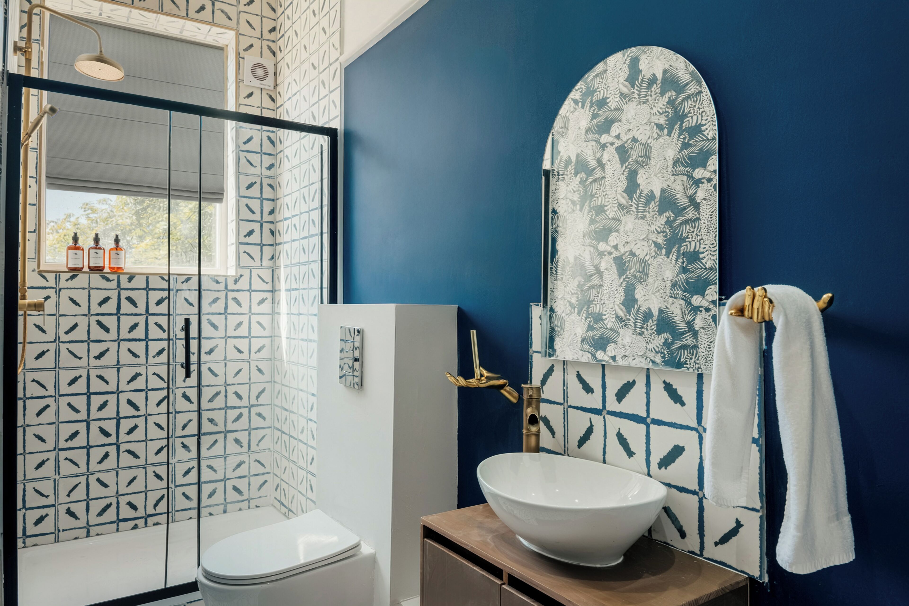 A bathroom with a white toilet, a large white sink, a shower with a glass door, and a blue wall with a floral pattern.
