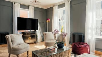 A living room with a flat-screen TV, two armchairs, a coffee table, and a red ottoman.