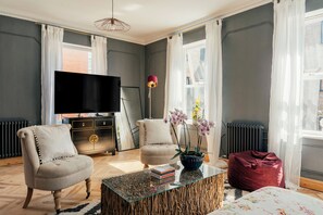 Un salon équipé d’un téléviseur à écran plat, de deux fauteuils, d’une table basse et d’un pouf rouge.