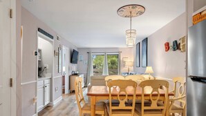 A dining area with a wooden table and chairs, a chandelier, and a view through a window. - Relaxing Beach Retreat Villa, Walk to Beach and Resort (Hilton Head)