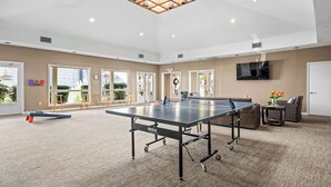 A spacious indoor area with a ping pong table, wicker furniture, and a large ceiling light fixture. - Relaxing Beach Retreat Villa, Walk to Beach and Resort (Hilton Head)