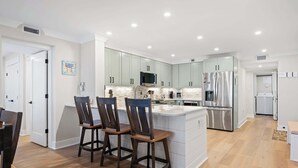 A modern kitchen with a central island, bar stools, and stainless steel appliances. - Luxury Direct Oceanfront 3BR Panoramic Ocean Views (Hilton Head Island)