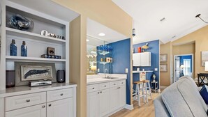 A modern kitchen with white cabinetry, a built-in oven, and a dining area with a gray sofa and wooden stools. - Beautiful & Spacious Golf View Villa Next to Pool (Hilton Head)