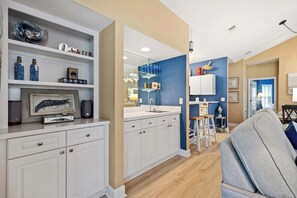 A modern kitchen with white cabinetry, a built-in oven, and a dining area with a gray sofa and wooden stools. - Beautiful & Spacious Golf View Villa Next to Pool (Hilton Head)