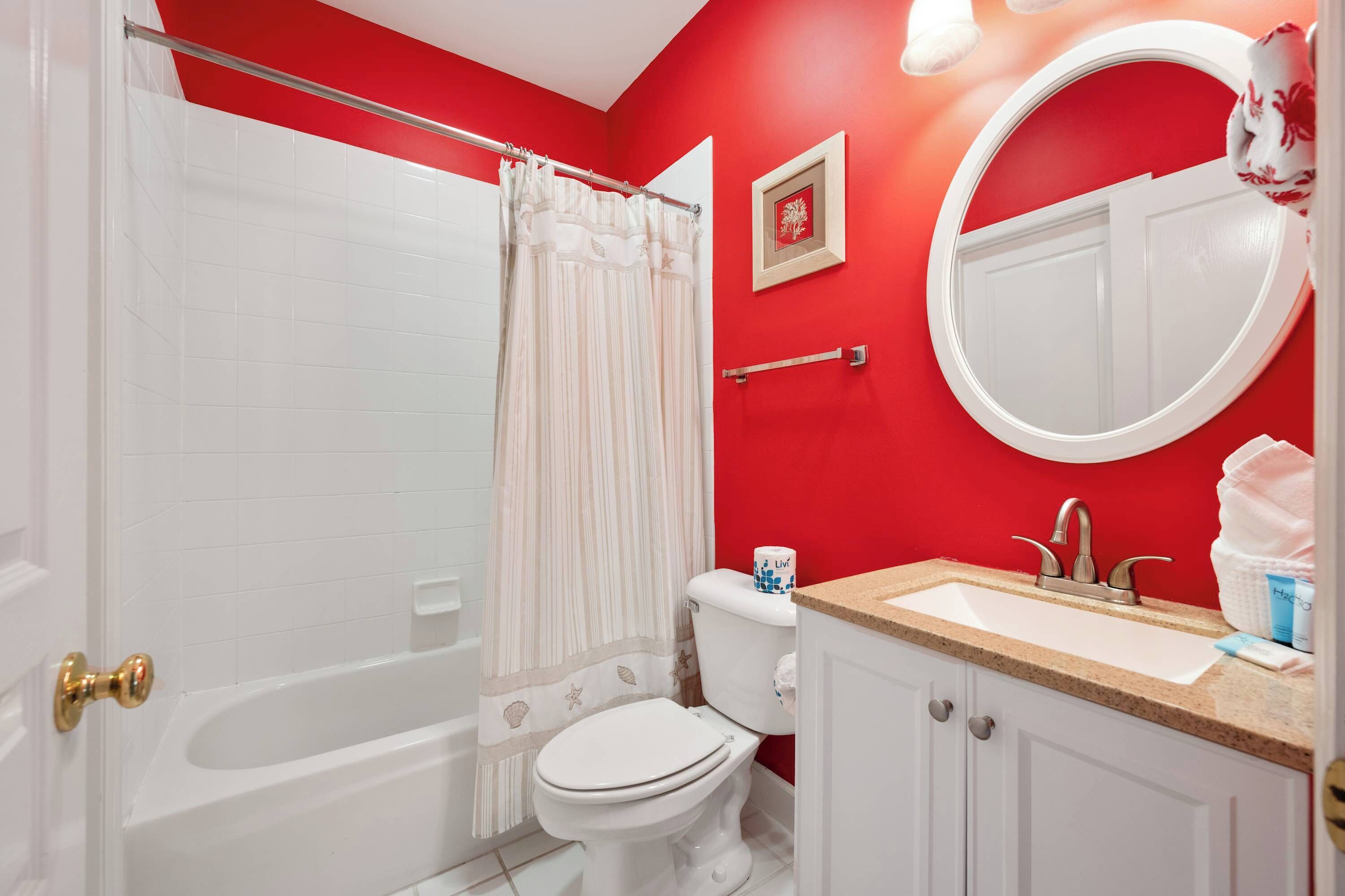 A bathroom with a white bathtub, toilet, and sink, red walls, and a white door.