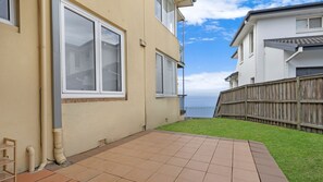 Ein Wohnhaus mit gepflasterter Terrasse, Holzzaun und Blick auf das Meer.