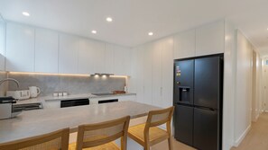 Eine moderne Küche mit weißen Schränken, einer zentralen Kochinsel, einem schwarzen Kühlschrank und zwei Holzstühlen.