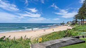 Una spiaggia con un cartello di avvertimento, onde oceaniche e edifici sullo sfondo.