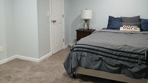 Quarto com cama, mesa de cabeceira, abajur e porta.