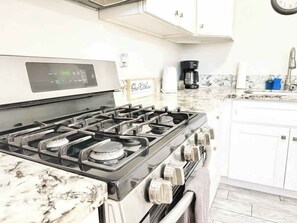 Una cocina con estufa, alacenas y cafetera.