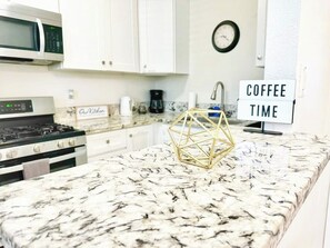Eine Küche mit Marmorarbeitsplatte, einem Schild mit der Aufschrift 'Kaffee' und einer Uhr, sowie einem Schild mit dem Schriftzug 'Unsere Küche'.