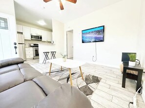Ein modernes Wohnzimmer mit einer Couch, einem Esstisch und einem an der Wand befestigten Fernseher.