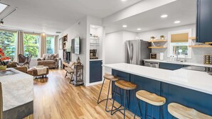 A modern kitchen with a large island, bar stools, and a dining area with a sofa and chairs. - Verdant Falls! Hot Tub & Mtn Views near Broadmoor (Colorado Springs)