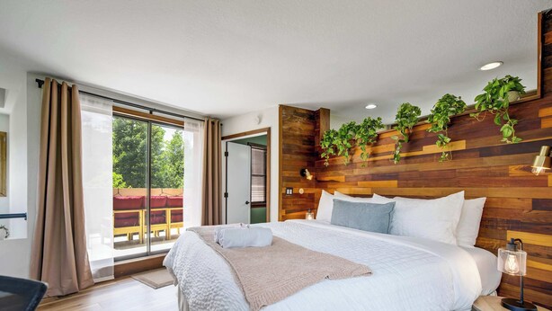 A bedroom with a large bed, wooden panel wall, and a view to the outside. - Verdant Falls! Hot Tub & Mtn Views near Broadmoor (Colorado Springs)