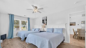 Ein Hotelzimmer mit zwei Betten, einem Deckenventilator, einem Essbereich mit Korbstühlen und Blick ins Freie durch das Fenster.