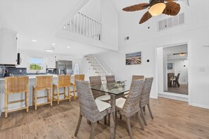 A spacious kitchen with white cabinetry, a dining area with wicker chairs, and a staircase leading to an upper level. - Private Dock and walk to beach. 4-bedroom house in beautiful OIB (Ocean Isle Beach)