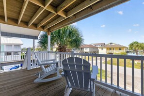 A wooden deck with a rocking chair and a white fence overlooking a residential area with houses and palm trees. - Private Dock and walk to beach. 4-bedroom house in beautiful OIB (Ocean Isle Beach)