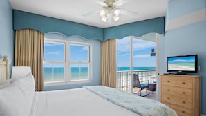 Ein Hotelzimmer mit Bett, Fernseher, Schminktisch und einem Balkon mit Blick auf den Strand.