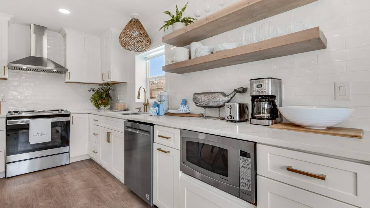 Una cocina moderna con armarios blancos, electrodomésticos de acero inoxidable y estantes de madera.