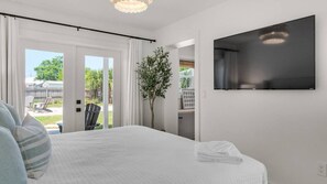Ein Schlafzimmer mit einem Bett, einem Fernseher, einer Pflanze und Blick ins Freie.