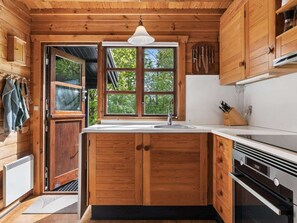 A wooden cabin kitchen with a large window, wooden cabinets, a sink, and a stove. - 4 Star Holiday Home in Roslev (Roslev)