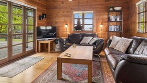 En stuga med träpanel på insidan, ett träpanelat tak, en tv, lädersoffor, ett soffbord och en bokhylla.