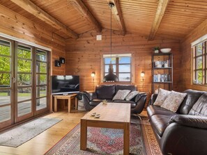 A log cabin interior with a wooden ceiling, a television, leather sofas, a coffee table, and a bookshelf. - 4 Star Holiday Home in Roslev (Roslev)