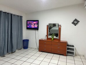 A room with a television, a dresser, a mirror, a clock, and a blue basket. - Casa Tonala 3 Rec. Wifi.A/c. FIFA 2026/GDL AirPort (Tonalá)