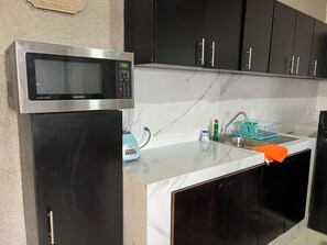 Una cocina con microondas, licuadora, fregadero y armarios negros.
