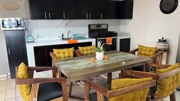 A modern kitchen with black cabinets, a wooden dining table with yellow cushioned chairs, a clock on the wall, and a kettle on the counter.