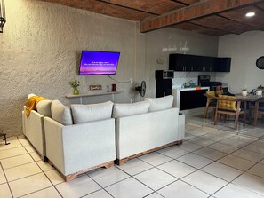 Ein Wohnzimmer mit Sofa, Fernseher, Küchenzeile und Esstisch.