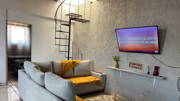 A living room with a sofa, a TV mounted on the wall, a small shelf with decorative items, and a patterned rug. - Casa Tonala 3 Rec. Wifi.A/c. FIFA 2026/GDL AirPort (Tonalá)