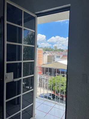 Vista desde un balcón con barandilla metálica, piso de baldosas y cielo despejado con nubes.