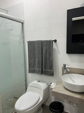 Ein Badezimmer mit Toilette, Waschbecken, Handtuchhalter und einer Duschkabine aus Glas.