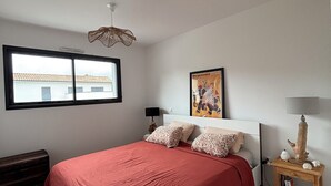 Een slaapkamer met een groot bed, een raam, een nachtkastje met een lamp en een wandkunstwerk.