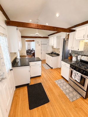 A kitchen with wooden floors, white cabinets, a stove, and a ceiling fan.