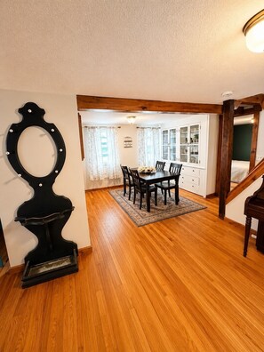 A dining area with a wooden floor, a dining table with chairs, a black decorative object, and a staircase leading to another room.