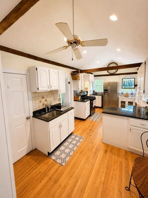 A kitchen with white cabinets, a black countertop, a ceiling fan, and a refrigerator.