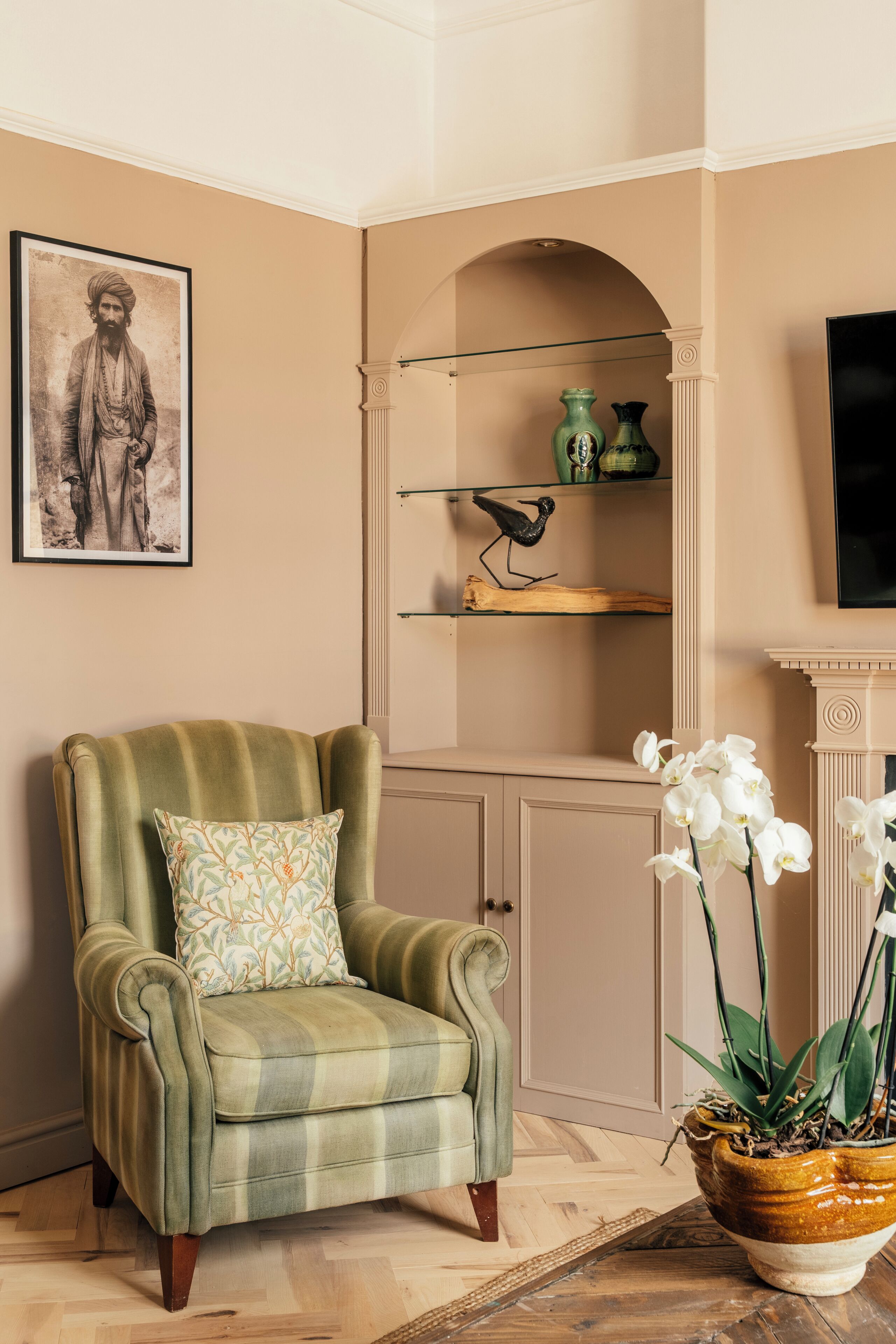 Ein Zimmer mit einem grünen Sessel, einem gerahmten Porträt, einer Ablage mit Dekoration und einem Topf mit einer Orchidee.