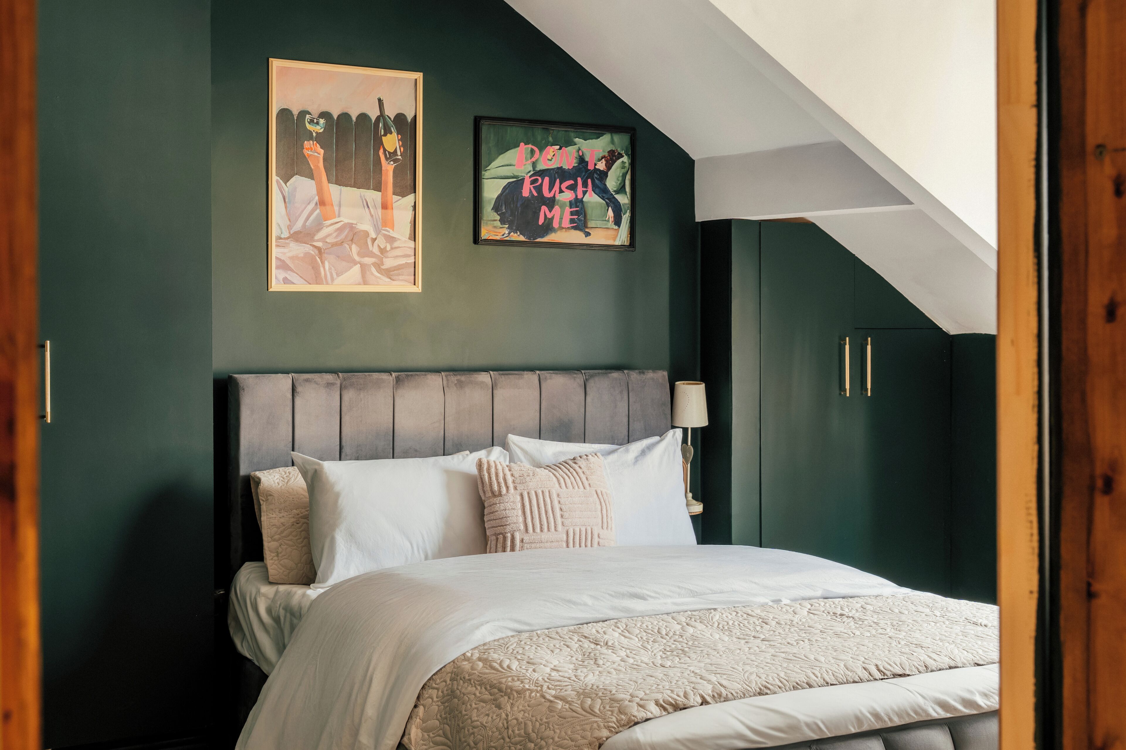 Un dormitorio con cama, cabecera, lámpara de pared y dos cuadros enmarcados.