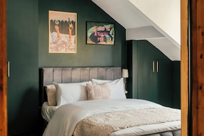 Ein Schlafzimmer mit einem Bett, einem Kopfteil, einer Wandleuchte und zwei gerahmten Bildern.