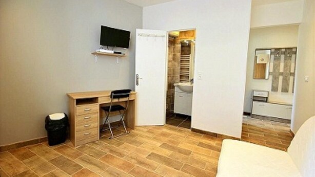 A bedroom with a bed, a desk, a chair, a television, and a bathroom with a sink and mirror. - Le palais du soleil (Cannes)