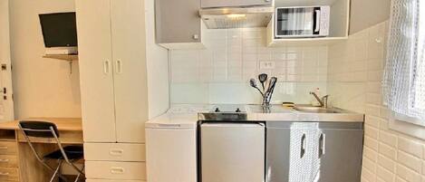 A compact kitchen with white cabinets, a built-in microwave, and a small refrigerator.