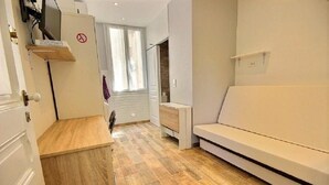 A room with a wooden floor, a white sofa, a small table, and a door with a sign. - Le palais du soleil (Cannes)