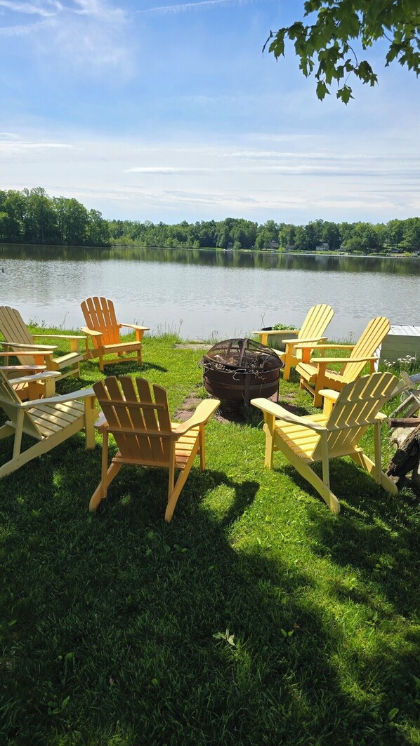 A lakeside setting with Adirondack chairs arranged around a fire pit.