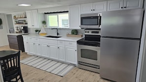 A modern kitchen with white cabinets, a stainless steel refrigerator, a microwave, and an oven.