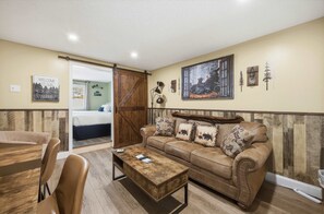 A cozy living room with a brown leather sofa, a wooden coffee table, and a sliding barn door leading to a bedroom. - Eastern Inn Deer Meadow Suite for 4 (North Conway)